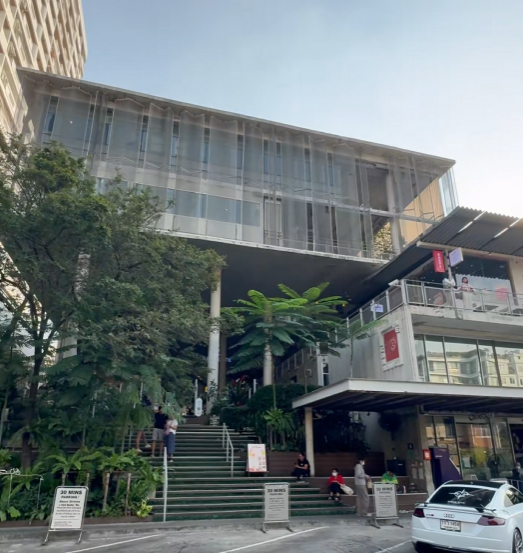 ภาพภายนอกของ The Commons Thonglor แสดงพื้นที่ถอยร่นบริเวณทางเข้า พื้นที่สีเขียวด้านหน้า และบันไดหลักที่เชื่อมขึ้นสู่ชั้นบน
